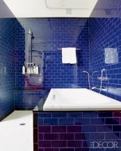 bold and glossy navy tiles with white grout plus a white bathtub for a bright and chic look