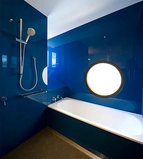 a minimalist and sleek bright blue bathroom plus a gold floor and a white tub