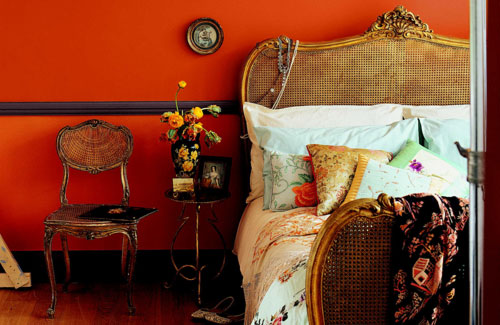 a bold orange bedroom with a bed with a woven headboard, bright printed bedding, vintage furniture is a bright and chic space