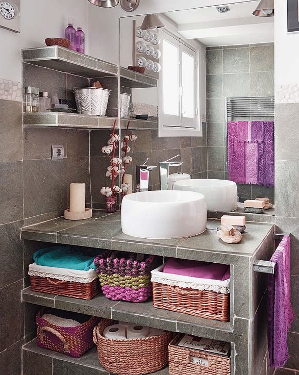 A grey bathroom clad with sotne like tiles and with bright towels and other textiles