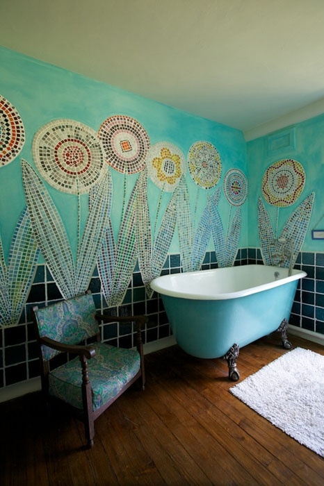 A creative bathroom with turquoise walls done with mosaic florals for a free spirited feel, a bright clawfoot tub and a vintage chair