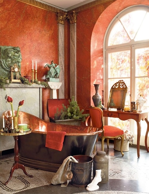 an elegant vintage bathroom with red plaster walls, a black and copper tub, chic sculptures and a vintage console table