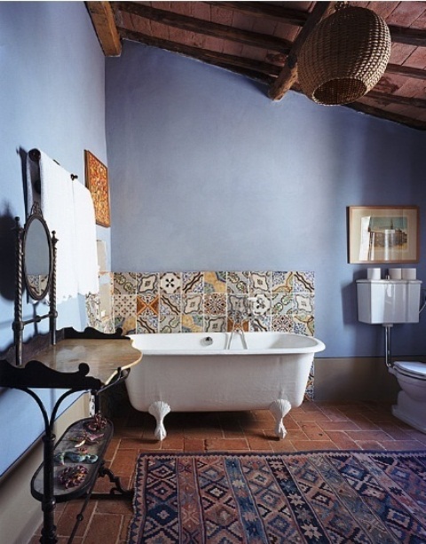 a vintage boho bathroom with blue walls, a clawfoot tub, boho rugs and Moroccan tiles, a carved wooden vanity and an ornate mirror
