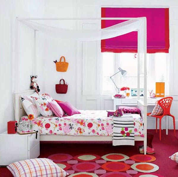 A contrasting girl's bedroom in white, with a canopy bed and super bold fuchsia and red textiles for an accent, with a red chair, pillows and rugs and bright bags