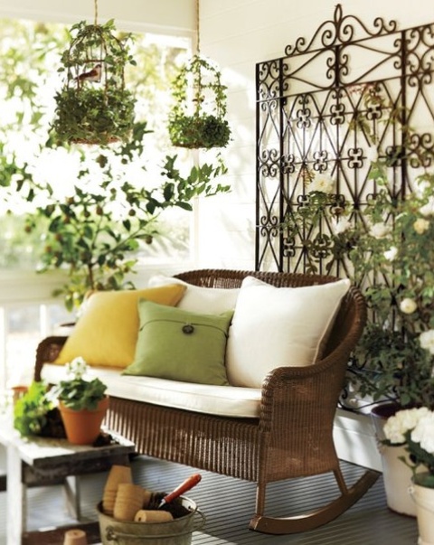 a refined vintage spring terrace with a forged screen, greenery and blooms, a wicker bench and bold pillows, greenery cages and potted greenery