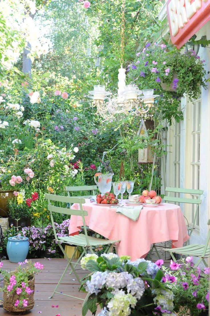 A bloom filled spring terrace with potted greenery and flowers all around, with a dining set, a chandelier and some fresh fruit