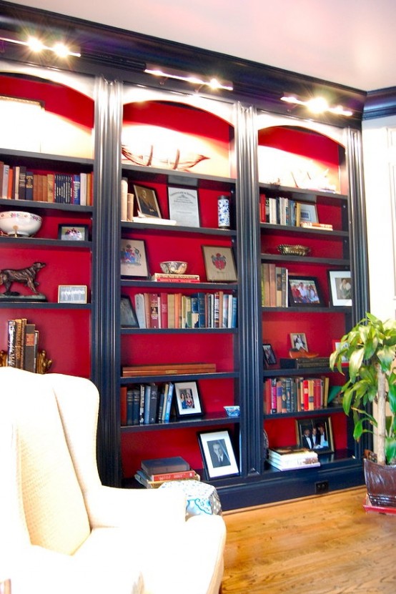 stylish navy built-in bookshelves with red backing and additional lights over the shelves are amazing for a refined space