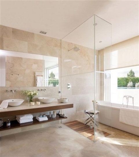 A modern tan colored bathroom with a floating open shelf vanity, a large mirror, a shower space and a bathtub by the window