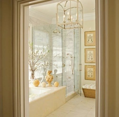 A neutral bathroom with a built in tub clad with marble, a shower space, a gallery wall and a vintage chandelier