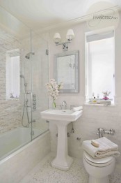 a refined neutral modern bathroom clad with various types of tiles, a free-standing sink and white appliances plus a mirror and a sconce over the mirror