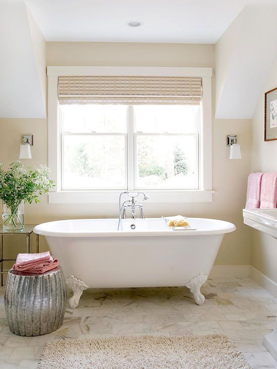 A welcoming warm colored bathroom with tan walls, a clawfoot tub and a shiny metallic side table plus pink towels