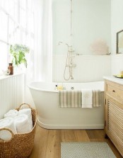 a neutral farmhouse bathroom with beadboard panels, a wooden vanity, a free-standing tub and a basket with towels