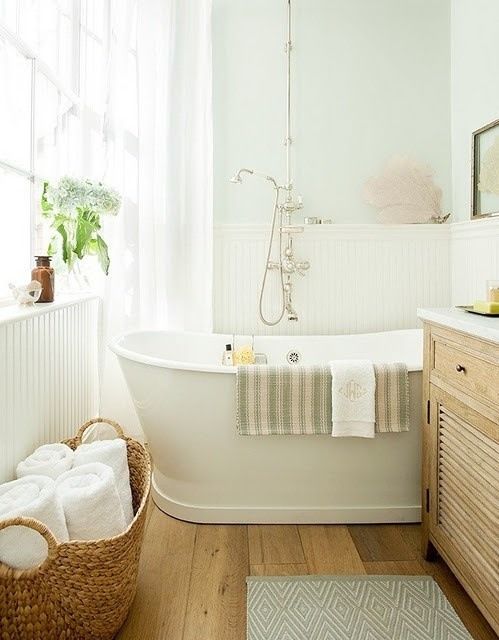 A neutral farmhouse bathroom with beadboard panels, a wooden vanity, a free standing tub and a basket with towels