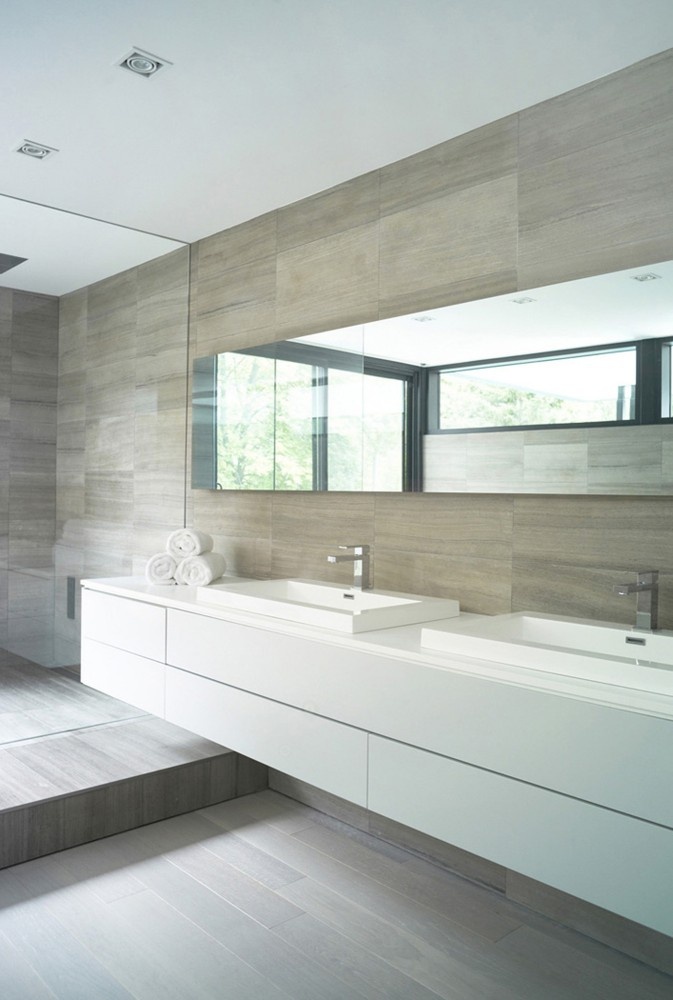 A neutral bathroom clad with wood like tiles, with a sleek floating vanity, a long mirror and some square sinks