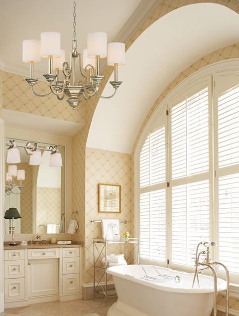 A neutral and warm colored bathroom with a glazed wall, a vintage tub, a vintage chandelier, a built in vanity and a mirror