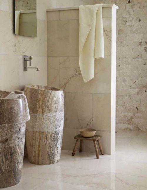 a refined neutral bathroom with mismatching tiles, free-standing sinks carved out of stone, a shower space and a mirror
