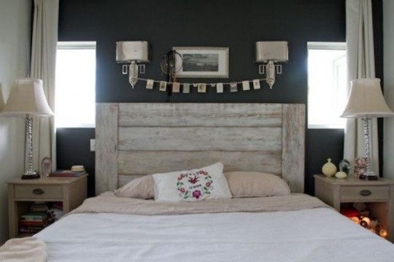 a farmhouse bedroom with black walls, a bed with a whitewashed headboard, neutral nightstands and table lamps, sconces and artwork