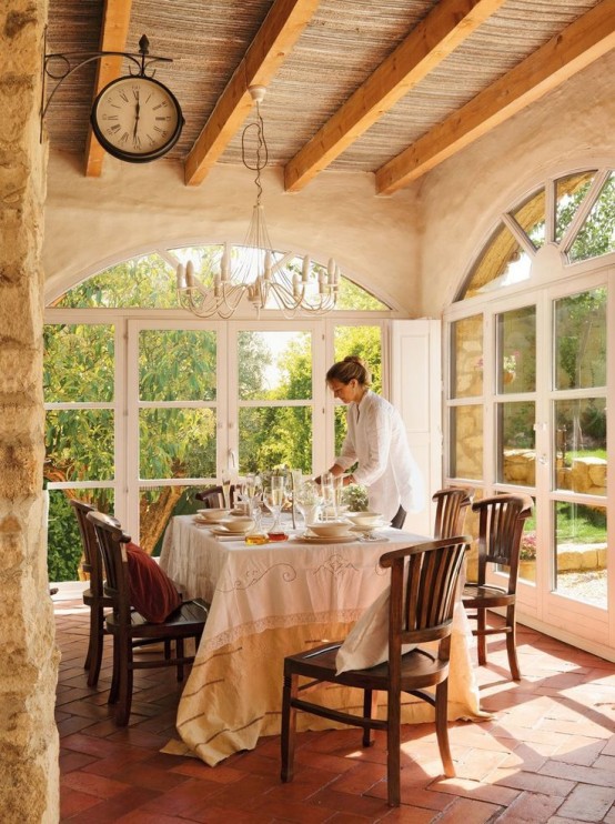 a rustic Provence dining space with large arched windows, a table and dark-stained chairs, a vintage chandelier and a clock on the wall