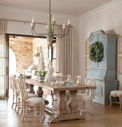 a lovely Provence dining room with a blue storage unit, a stained table and neutral vintage chair. a chandelier and an entrance to the sunroom