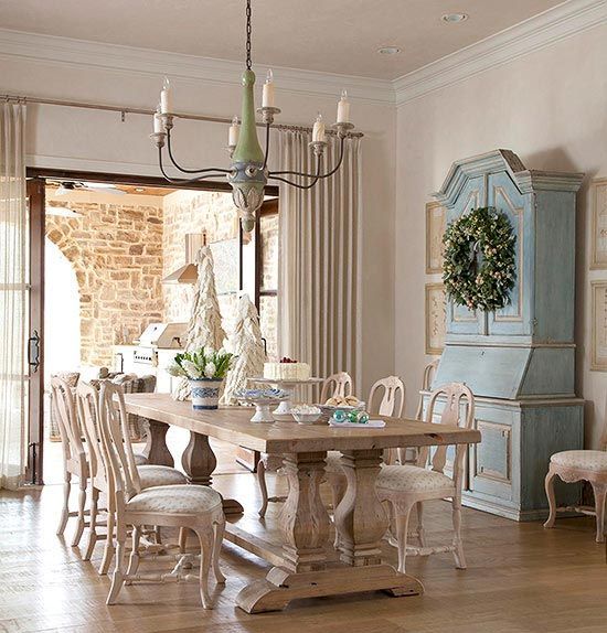 a lovely Provence dining room with a blue storage unit, a stained table and neutral vintage chair. a chandelier and an entrance to the sunroom