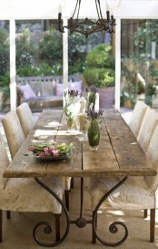 a rustic Provence dining room with a stained table, refined vintage chairs, a vintage chandelier and a glazed wall with a garden view