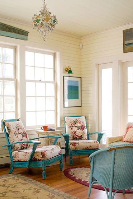 a vintage coastal sunroom with blue furniture, floral upholstery, a bright chandelier and an artwork