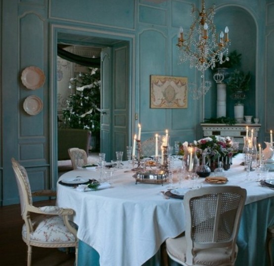 a refined and chic French dining room with blue walls, a white fireplace, a table and neutral vintage chairs, a crystal chandelier