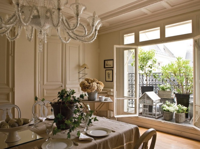 A beautiful neutral French dining room with paneling, a table and chic vintage chairs, a beautiful chandelier and a large window to enjoy the views