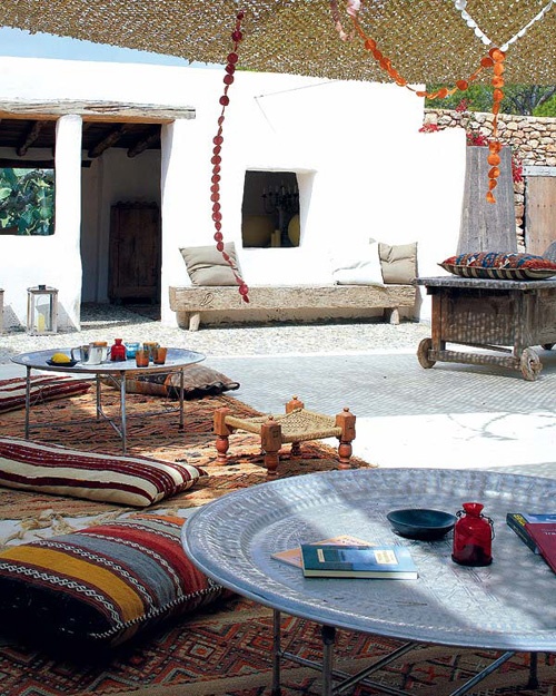 a bright Moroccan patio with colorful printed rugs and pillows, low metal tables and colorful glasses