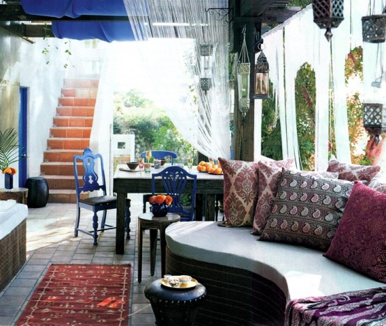 a bright Moroccan space with a curved sofa, Moroccan lanterns over it, a wooden table and bright blue chairs