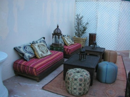 a bright Moroccan patio with colorful furniture, leather ottomans and a low coffee table