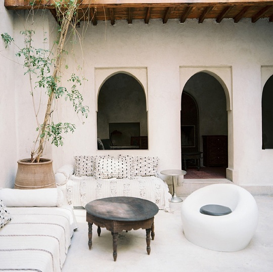 a white Moroccan patio with contemporary furniture, a low wooden table and potted greenery