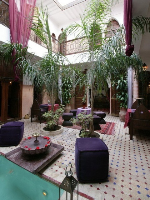 a refined Moroccan patio with a tiled floor, deep purple furniture and carved items plus a fountain
