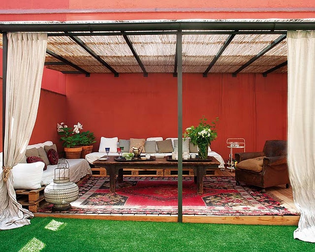 a bright red patio with curtains, pallet sofas and a table plus Moroccan rugs and lanterns
