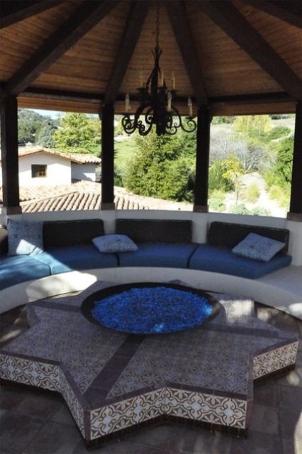 a roofed Moroccan patio done with a rounded bench, a star-shaped stand and a fire pit
