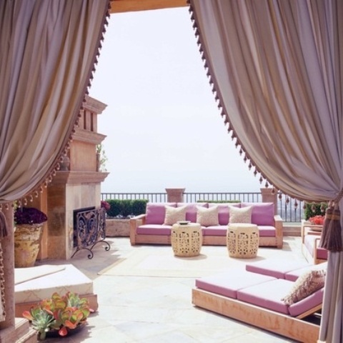 a colorful Moroccan patio with bright pnk textiles, carved siddde tables and touches of ivory