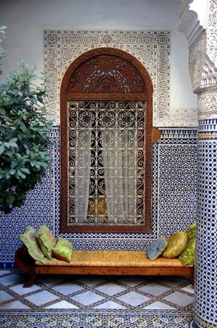 a Moroccan patio clad with mosaic blue and white tiles, a carved window frame and a bright daybed