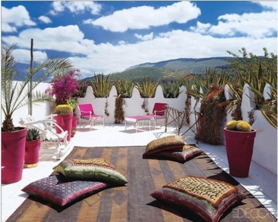 a bright rooftop terrace with greenery in colorful pots, pink loungers and colorful textiles