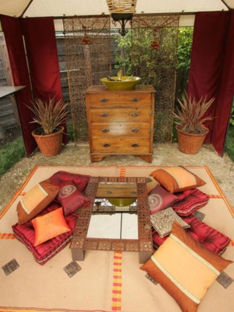 a warm-colored Moroccan patio in sandy beige and red, with pillows, rugs and a low table with a mirror in the center