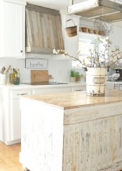 a shabby chic farmhouse kitchen in neutrals, with a shabby kitchen island, white cabinets and a weathered wood hood