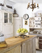 a shabby chic kitchen with neutral furniture, a kitchen island with burlap covering it, white cabinets, a vintage chandelier and some vintage decor