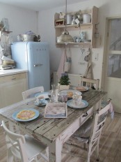 a neutral shabby chic kitchen with neutral and pastel furniture, a pastel blue fridge, a shabby chic table and chairs and printed linens