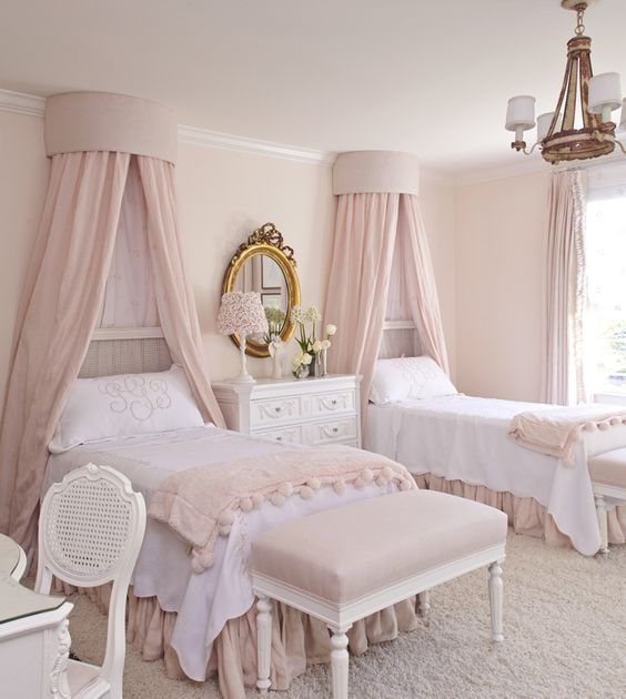 A delicate princess style blush shared bedroom with vintage beds with blush canopies and bedding, poufs, a desk and a chair is just gorgeous