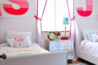 a colorful shared girls’ bedroom with creamy upholstered beds, colorful bedding, a bright rug, pink to red ombre monograms, a gold polka dot ceiling for a touch of fun