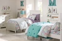a white shared girls’ bedroom with white vintage furniture, colorful printed bedding, gallery walls and white baskets for storage under the beds