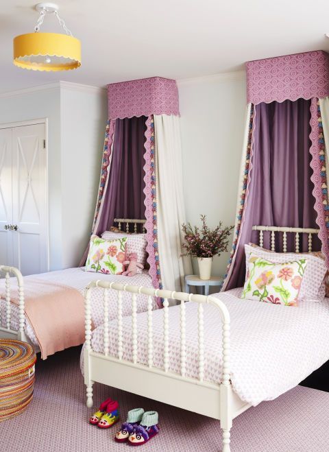 A chic and stylish shared girls' bedroom with white vintage beds, lilac and peachy bedding, purple canopies, a built in wardrobe and a woven basket for storage