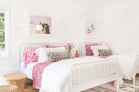 a chic neutral boho shared girls’ bedroom with white wooden beds, a bright printed rug, pink bedding, wooden side tables, faux fur and blooms