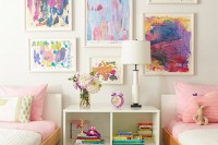 a pretty shared girls’ bedroom with a bright watercolor gallery wall, sleek white beds with colorful bedding, a white nightstad and a white table lamp is wow