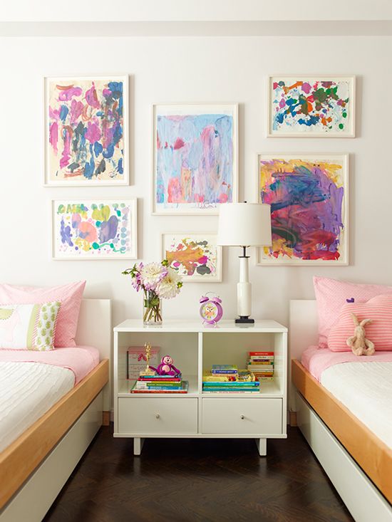 a pretty shared girls' bedroom with a bright watercolor gallery wall, sleek white beds with colorful bedding, a white nightstad and a white table lamp is wow