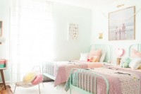 a neutral light-filled bedroom with mint-colored beds, colorful bedding and pillows, artworks, a desk and some chairs is a stylish and cool space